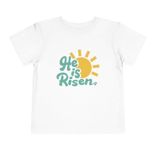 Child wearing a blue knit hat and a 'He is Risen' t-shirt on a white background
