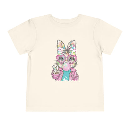 Beige t-shirt with a colorful cartoon bunny holding a peace sign on a white background