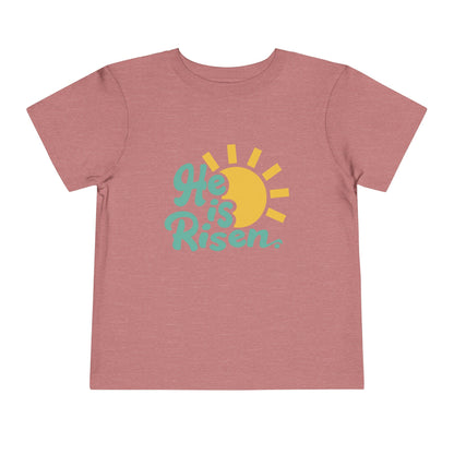 Pink t-shirt with 'He is Risen' design featuring a sun on a white background