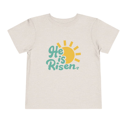 Beige t-shirt with 'He is Risen' text and sun graphic on a white background