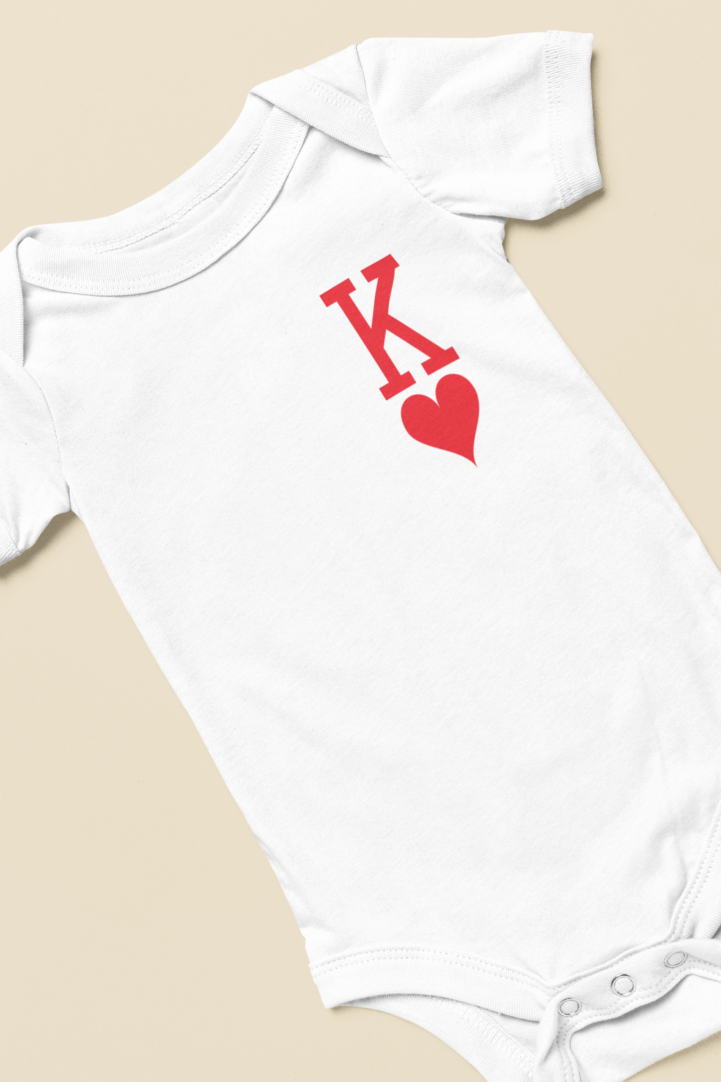 White baby onesie with red letter 'K' and heart design on a beige background