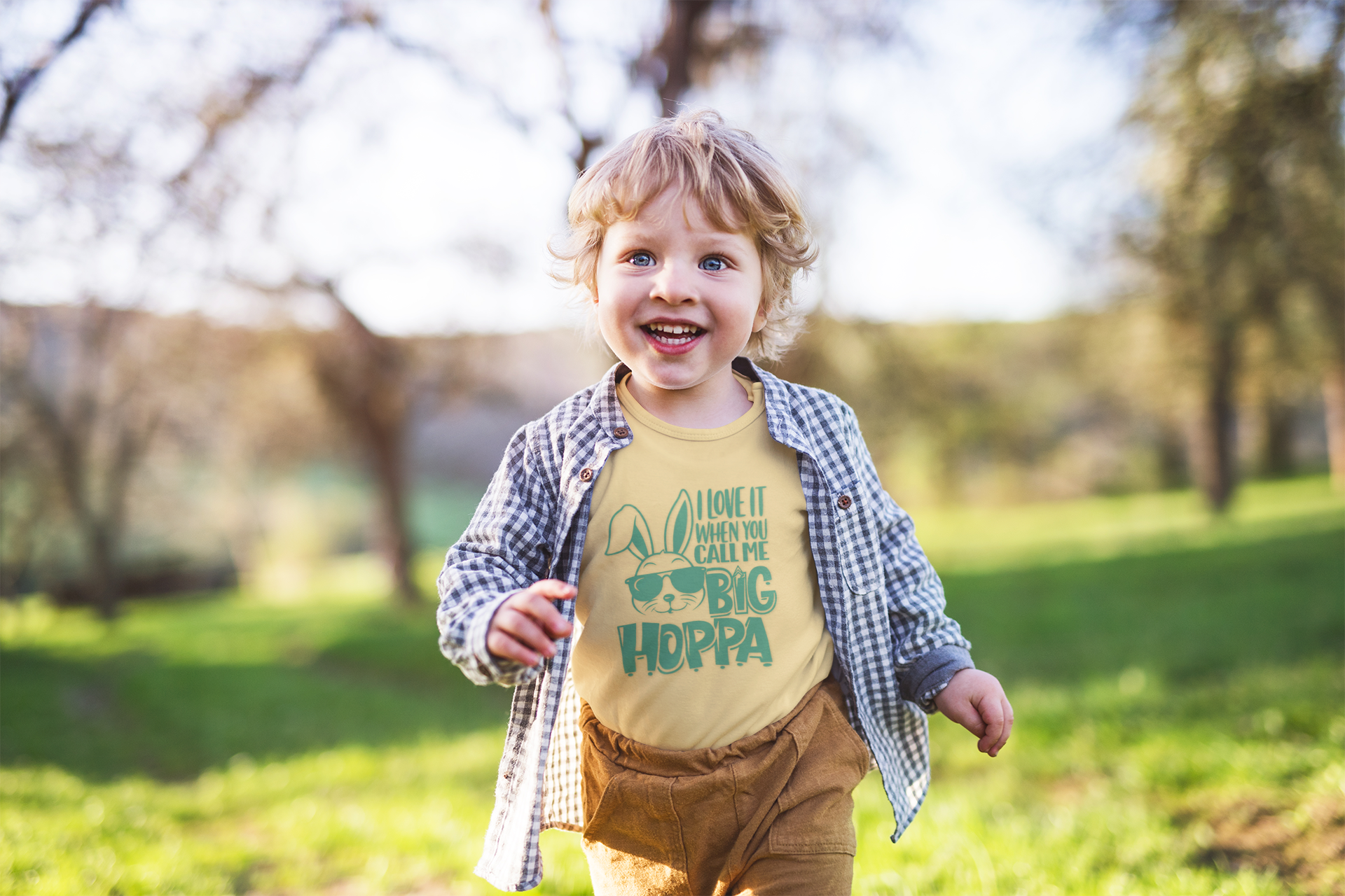 Child wearing a yellow shirt with text, standing outdoors in a park.
