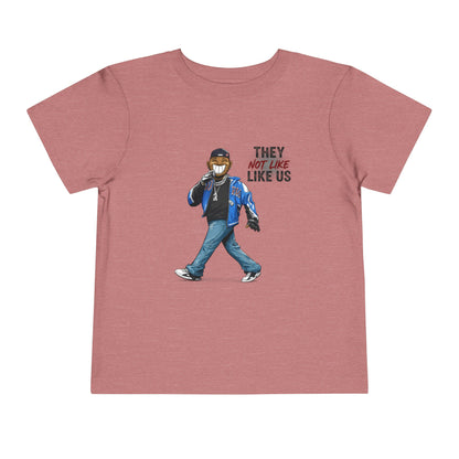 Pink t-shirt with graphic of a person wearing a mask and text 'THEY LIKE NOT US LIKE US' on a white background