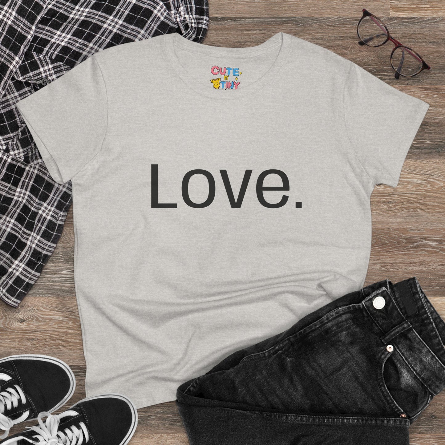 Pink t-shirt with a graphic design of a heart, hands, and flowers on a wooden surface with clothing items.